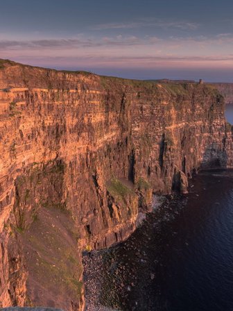 Die beeindruckenden Cliffs of Moher erheben sich majestätisch über den ruhigen Atlantik, beleuchtet von warmem Abendlicht.