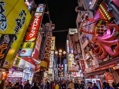 Bunte Neonlichter erhellen eine belebte Straße in Osaka, gesäumt von Geschäften und einem riesigen, pinken Oktopus.