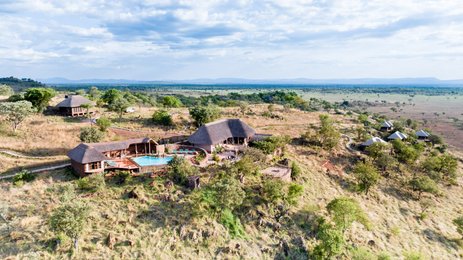 Eine atemberaubende Aussicht auf die Ikoma Hills Lodge, umgeben von sanften Hügeln und üppiger Vegetation in Tansania.