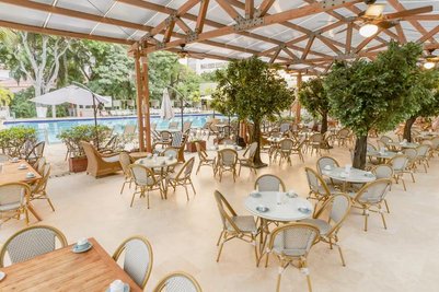 Ein einladender Außenbereich mit Tischen und Stühlen, umgeben von Bäumen, bietet einen Blick auf den Pool im Hintergrund.