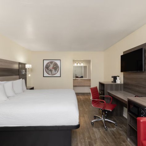 Ein modernes Hotelzimmer mit einem großen Bett, einem Schreibtisch und einem roten Stuhl, ideal für Geschäftsreisende.
