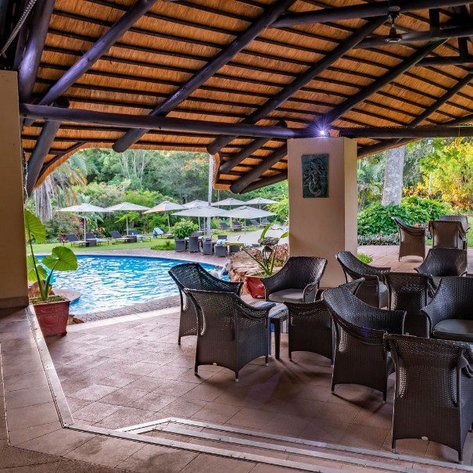 Ein einladender Poolbereich mit gemütlichen Stühlen und Sonnenschirmen, umgeben von üppigem Grün und einem schützenden Dach.