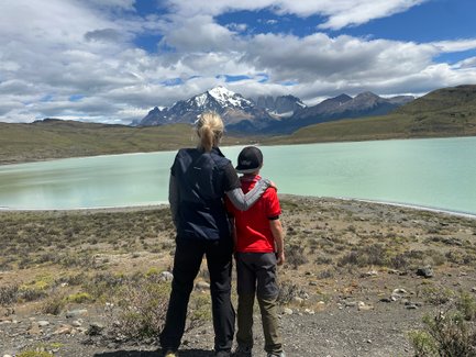 Eine Frau und ein Junge stehen am Ufer eines türkisfarbenen Sees und blicken auf die majestätischen Berge im Hintergrund.