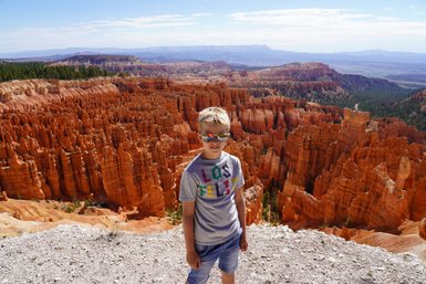 Ein Junge mit Sonnenbrille steht vor den beeindruckenden, orangefarbenen Felsformationen des Bryce Canyon Nationalparks.