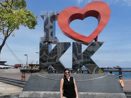 Frau steht vor dem berühmten Kota Kinabalu Schriftzug und genießt den Ausblick auf die Küste – Malaysia & Borneo mit Kindern