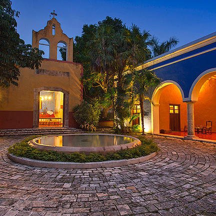 Ein malerischer Innenhof mit einem runden Brunnen, umgeben von üppigem Grün und historischen Gebäuden in sanften Farben.