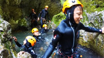 Eine Gruppe von Abenteurern in Neoprenanzügen erkundet einen schmalen, moosbedeckten Canyon mit klarem Wasser.