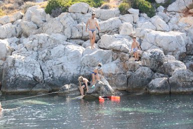Eine Familie genießt einen sonnigen Tag am Meer, während Kinder auf den Felsen spielen und im Wasser planschen.