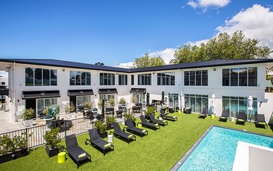 Ein modernes Boutique-Hotel mit einem einladenden Poolbereich und Liegen auf grünem Rasen unter blauem Himmel.
