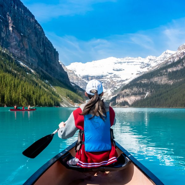 Eine Person paddelt in einem Kanu auf dem türkisfarbenen Wasser des Lake Louise, umgeben von majestätischen Bergen.