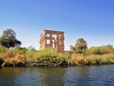 Die ruins of the Philae-Tempel erheben sich majestätisch über das grüne Ufer des Nils, umgeben von üppigem Grün und Palmen.