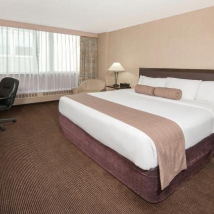 Ein modernes Hotelzimmer mit einem großen Doppelbett, einem Schreibtisch und einem bequemen Stuhl, ideal für Geschäftsreisende.