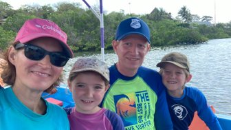 Eine Familie posiert fröhlich auf einem Boot, umgeben von üppigem Grün und Wasser, während sie einen Ausflug genießen.