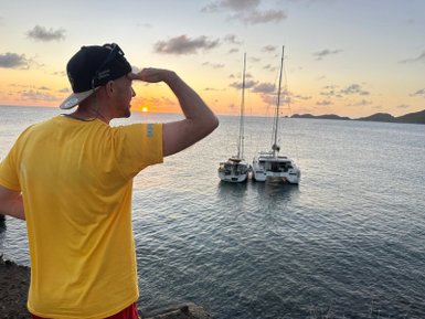 Ein Mann in einem gelben T-Shirt schaut in die Ferne, während die Sonne über dem Wasser untergeht.
