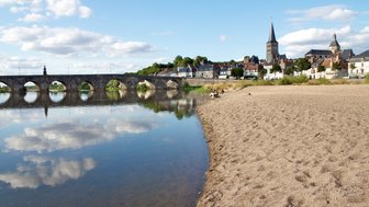 Ein ruhiger Strandabschnitt mit feinem Sand, der sanft ins Wasser übergeht, während Wolken sich im klaren Wasser spiegeln.