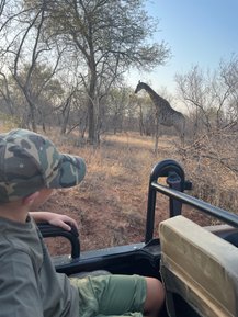 Ein Junge schaut fasziniert aus dem Safari-Jeep auf eine Giraffe im Kruger Nationalpark – Südafrika Reise mit Kindern