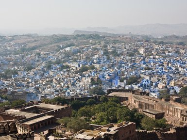 Eine weite Aussicht auf die blaue Stadt, umgeben von sanften Hügeln und historischen Festungsmauern im Vordergrund.