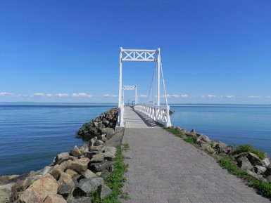 Eine malerische Seebrücke erstreckt sich über ruhiges Wasser, umgeben von sanften Wellen und einem strahlend blauen Himmel.