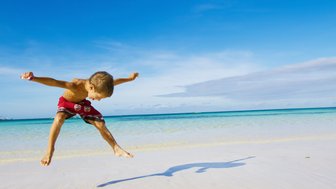 Junge springt am Sandstrand mit Blick auf das türkisfarbene Meer – Mexiko Reise mit Kindern