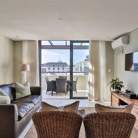 Ein modernes Wohnzimmer mit einem bequemen Sofa, einem Fernseher und einem großen Fenster, das auf einen Balkon blickt.