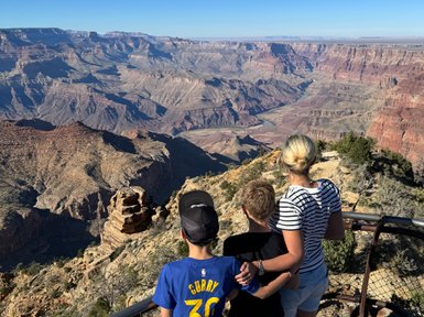 Drei Kinder stehen am Rand des Grand Canyon und bewundern die beeindruckende Aussicht auf die tiefen Schluchten und Felsen.