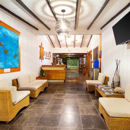 Der Empfangsbereich eines Hotels mit einem großen Gemälde einer Insel und modernen Sitzgelegenheiten aus Rattan.