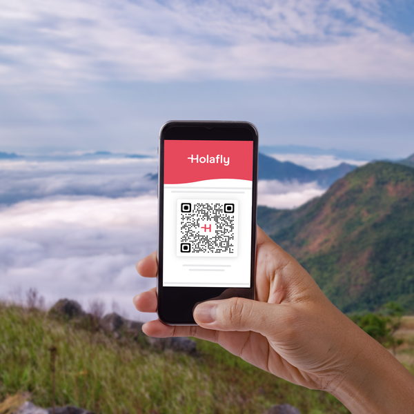 Ein Hand hält ein Smartphone mit einer QR-Code-Anzeige, umgeben von einer malerischen Berglandschaft.