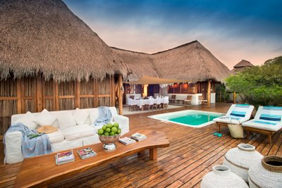 Eine stilvolle Terrasse mit einem Pool, umgeben von einem strohgedeckten Haus und gemütlichen Sitzgelegenheiten aus Holz.