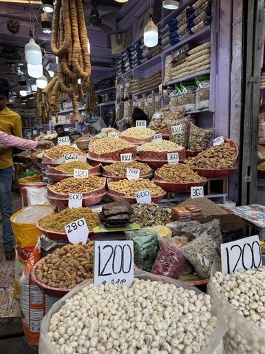 Ein lebhafter Gewürzmarkt mit bunten Töpfen voller Nüsse und Trockenfrüchte, umgeben von fröhlichen Verkäufern.