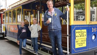 Eine Familie steht an einer Straßenbahn in San Francisco, lächelnd und bereit für ein Abenteuer in der Stadt.