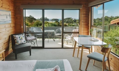 Ein gemütlicher Raum mit Holzverkleidung, einem Tisch und Stühlen, der einen Blick auf die Natur und das Meer bietet.