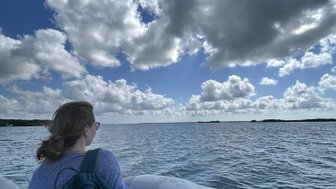 Eine Person sitzt in einem Boot und blickt auf das ruhige Wasser, umgeben von einer beeindruckenden Wolkenlandschaft.