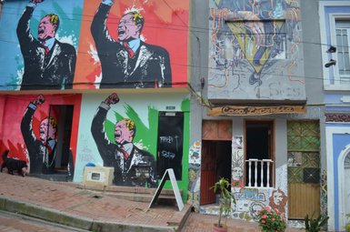 Bunte Graffiti an einer Wand zeigen einen leidenschaftlichen Redner mit erhobener Faust, umgeben von lebhaften Farben.