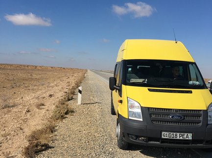Ein gelber Transporter steht auf einer einsamen Straße, umgeben von kargem, trockenem Gelände unter einem strahlend blauen Himmel.