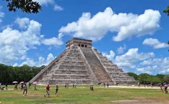 Die beeindruckende Pyramide von Chichén Itzá erhebt sich majestätisch unter einem strahlend blauen Himmel mit weißen Wolken.