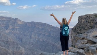 Frau steht auf einem Felsen und genießt die Aussicht über die Schluchten des Jebel Shams – Oman mit Kindern