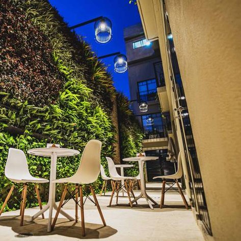 Ein stilvoller Außenbereich mit weißen Stühlen und Tischen, umgeben von üppigem Grün und sanfter Beleuchtung in der Dämmerung.