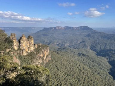 Die markanten Felsformationen der Three Sisters überragen die grüne Berglandschaft im blauen Himmel.
