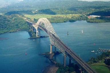Eine beeindruckende Brücke überspannt das Wasser, umgeben von üppigem Grün und sanften Hügeln im Hintergrund.
