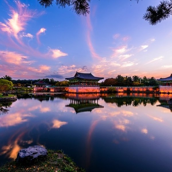 Ein malerischer Sonnenuntergang über dem Donggung Wolji Teich, mit reflektierenden Wolken und historischen Gebäuden im Hintergrund.