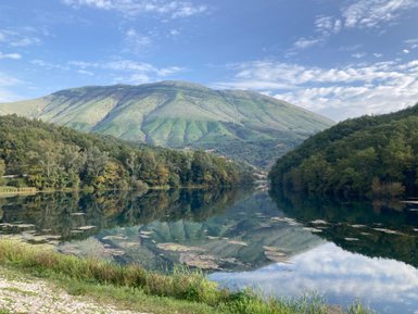 Ein ruhiger See spiegelt die sanften Hügel und den klaren Himmel wider, umgeben von üppigem Grün und sanften Wellen.