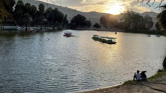 Am Ufer eines ruhigen Sees sitzen zwei Personen und genießen den Sonnenuntergang hinter den Sanddünen.