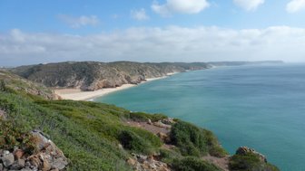 Eine atemberaubende Küstenlandschaft mit sanften Hügeln und klarem, blauem Wasser, das an einen goldenen Sandstrand plätschert.