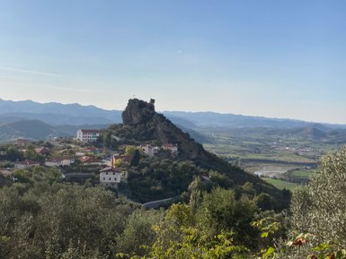 Eine malerische Landschaft mit einem Hügel, auf dem eine alte Festung thront, umgeben von grünen Tälern und Bergen.