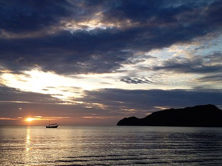 Ein Boot gleitet sanft über das ruhige Wasser, während die Sonne hinter dem Horizont untergeht und den Himmel in warmen Farben erleuchtet.