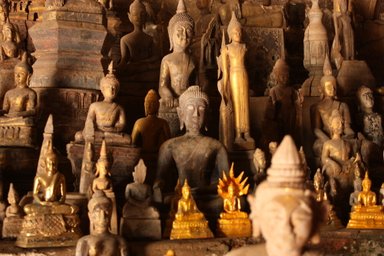 Eine Vielzahl von Buddha-Statuen in verschiedenen Größen und Stilen, die in einer dunklen Höhle angeordnet sind.