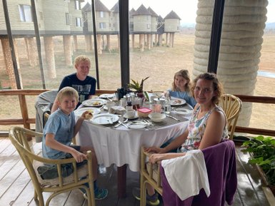 Eine Familie genießt ein Frühstück in einem Restaurant mit Blick auf die Taita Hills, umgeben von Natur und modernen Gebäuden.