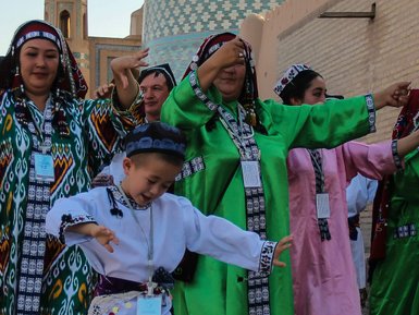 Eine Gruppe von Tänzern in traditionellen Kleidern tanzt fröhlich vor einer historischen Kulisse mit bunten Türmen.
