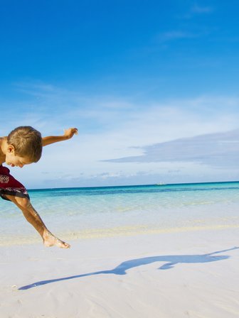 Junge springt am Sandstrand mit Blick auf das türkisfarbene Meer – Mexiko Reise mit Kindern