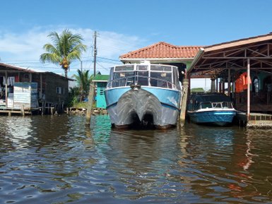 Zwei Boote liegen am Ufer eines ruhigen Gewässers, umgeben von bunten Holzhäusern und Palmen im Hintergrund.